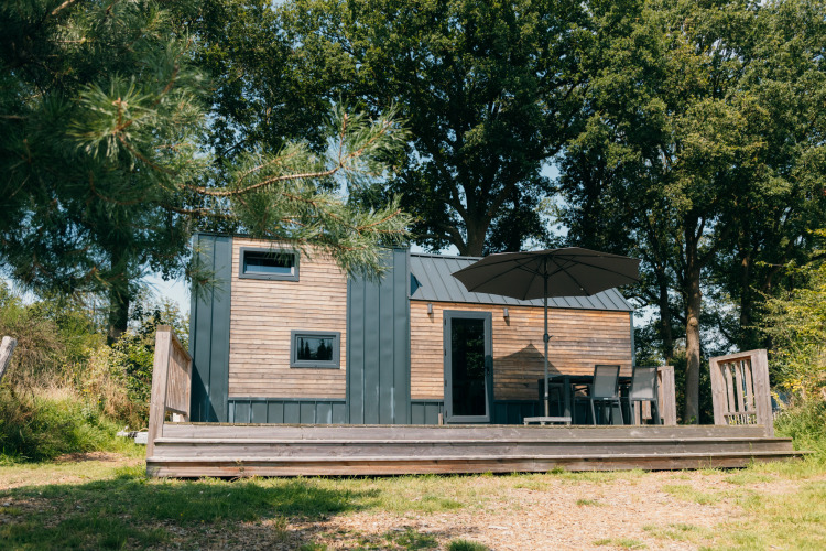 Kleines Holzhaus mit Terrasse und Sonnenschirm, umgeben von Bäumen, im Holiday Park Sallandshoeve, Niederlande.