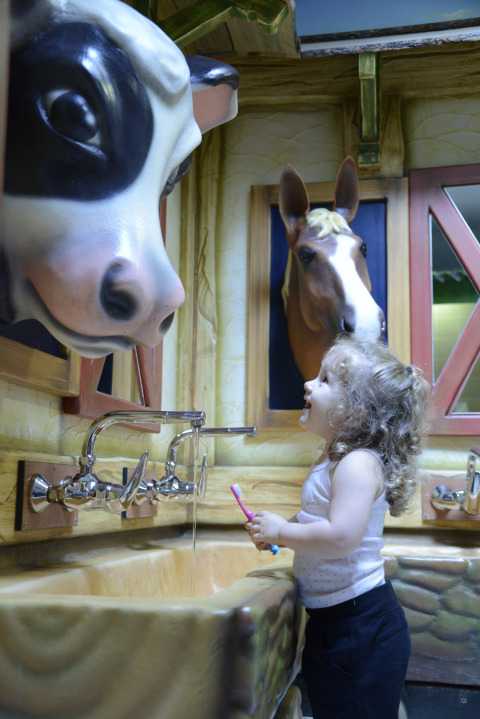 Un enfant se brosse les dents à un lavabo décoré de vache et de cheval au Camping Fuussekaul à Wiltz, Luxembourg.