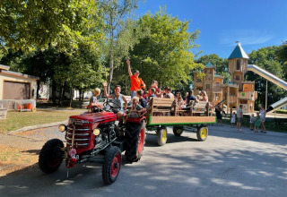 Niños y adultos disfrutan de un paseo en tractor junto al parque infantil de Camping Fuussekaul en Wiltz.