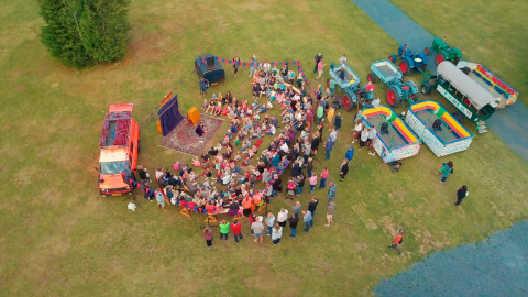 Aerial view of an outdoor event with crowds, colorful vehicles and stalls at Camping Fuussekaul, Wiltz.