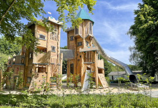 Large wooden playground castle with high towers and a slide at Camping Fuussekaul in Wiltz, Luxembourg.