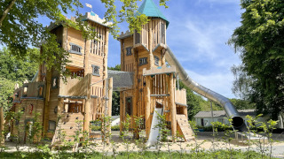 Grote houten speelburcht met glijbaan op het speelplein van Camping Fuussekaul in Wiltz, Luxemburg.