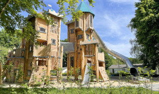 Castillo de madera en área de juegos con tobogán en Camping Fuussekaul, Wiltz, Luxemburgo.
