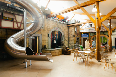 Indoor play area with spiral metal slide and seating at Camping Fuussekaul in Wiltz, Luxembourg.