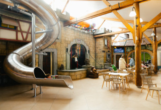 Area giochi interna con scivolo a spirale e tavoli al Camping Fuussekaul a Wiltz, Lussemburgo.