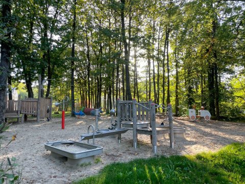 Parco giochi immerso negli alberi al Camping Fuussekaul di Wiltz, Lussemburgo, con sabbia e strutture ludiche.