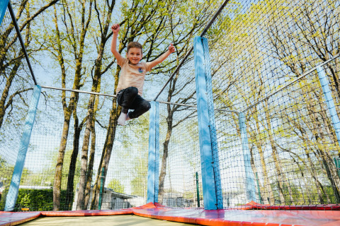 A child jumps joyfully on a trampoline outdoors at Camping Fuussekaul holiday park in Wiltz, Luxembourg.