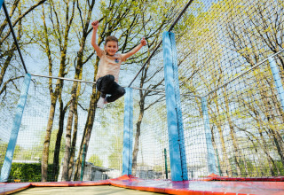 A child jumps joyfully on a trampoline outdoors at Camping Fuussekaul holiday park in Wiltz, Luxembourg.