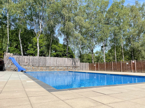 Piscina all’aperto con scivolo blu al Camping Fuussekaul, circondata da alberi a Wiltz, Lussemburgo.