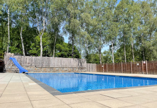 Piscina all’aperto con scivolo blu al Camping Fuussekaul, circondata da alberi a Wiltz, Lussemburgo.