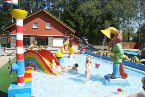 Children play in a colorful splash pool with slides and statues at Camping Fuussekaul, Wiltz, Luxembourg.