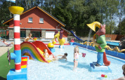 Children play in a colorful splash pool with slides and statues at Camping Fuussekaul, Wiltz, Luxembourg.
