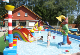 Children play in a colorful splash pool with slides and statues at Camping Fuussekaul, Wiltz, Luxembourg.