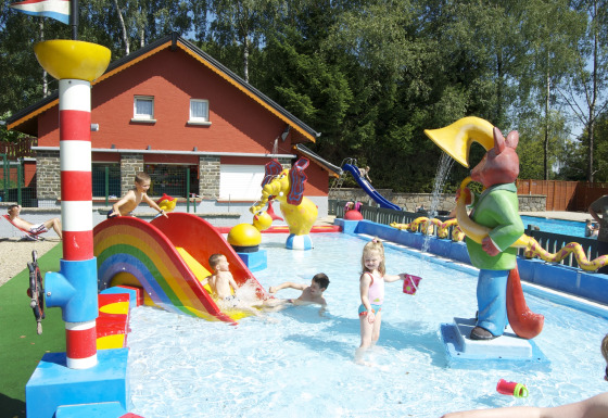 Bambini giocano in una piscina per bambini con scivolo e statue al Camping Fuussekaul, Wiltz, Lussemburgo.