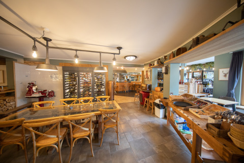 Interno della sala da pranzo al Camping Fuussekaul a Wiltz, Lussemburgo, con tavoli rustici e frigo per vini.