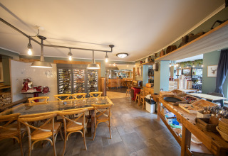 Interior de comedor en Camping Fuussekaul en Wiltz, Luxemburgo, con mesas de madera y nevera de vinos.