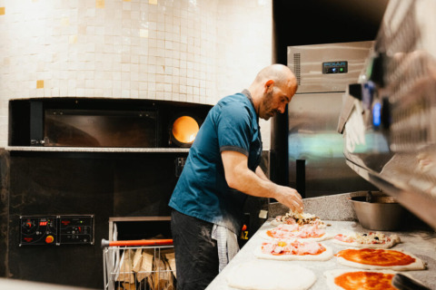 A chef prepares pizzas in a professional kitchen, a highlight of Camping Fuussekaul in Wiltz, Luxembourg.