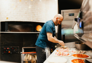 A chef prepares pizzas in a professional kitchen, a highlight of Camping Fuussekaul in Wiltz, Luxembourg.