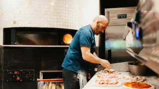 Een kok bereidt pizza's in een professionele keuken, een hoofdactiviteit op Camping Fuussekaul in Wiltz.