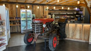 Café-interieur in Camping Fuussekaul met een rode oude tractor, drankkoelkasten en houten accenten.