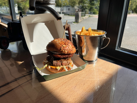 En burger og pommes frites serveret i en spand på et bord med udsigt fra Camping Fuussekaul i Wiltz, Luxembourg.