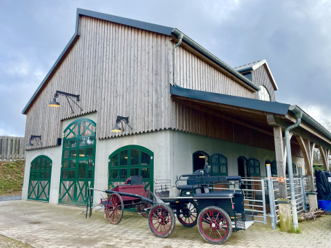 Edificio rustico con porte verdi e carrozze all’esterno al Camping Fuussekaul a Wiltz, Lussemburgo.