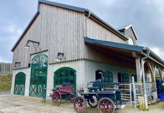 Edificio rustico con porte verdi e carrozze all’esterno al Camping Fuussekaul a Wiltz, Lussemburgo.