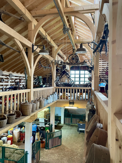 Rustic barn interior at Camping Fuussekaul, Wiltz, with wooden beams, baskets, and traditional farm tools.