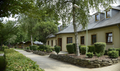 Pathway beside buildings and tents in lush greenery at Camping Fuussekaul holiday park in Wiltz, Luxembourg.