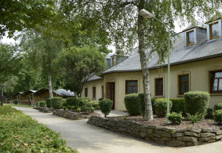 Pathway beside buildings and tents in lush greenery at Camping Fuussekaul holiday park in Wiltz, Luxembourg.