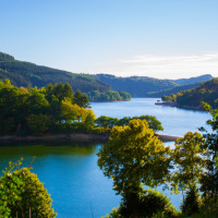 Mooi meer omgeven door groene bossen en heuvels aan een vakantiepark met glampingverblijven.