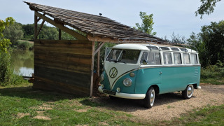 Foto di un furgone Volkswagen Combi d’epoca accanto a una baita in legno sul lago da Combi Harvey.