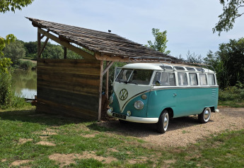 Ein Foto eines Retro-VW Combi neben einer Holzhütte am See bei Combi Harvey in der Natur.