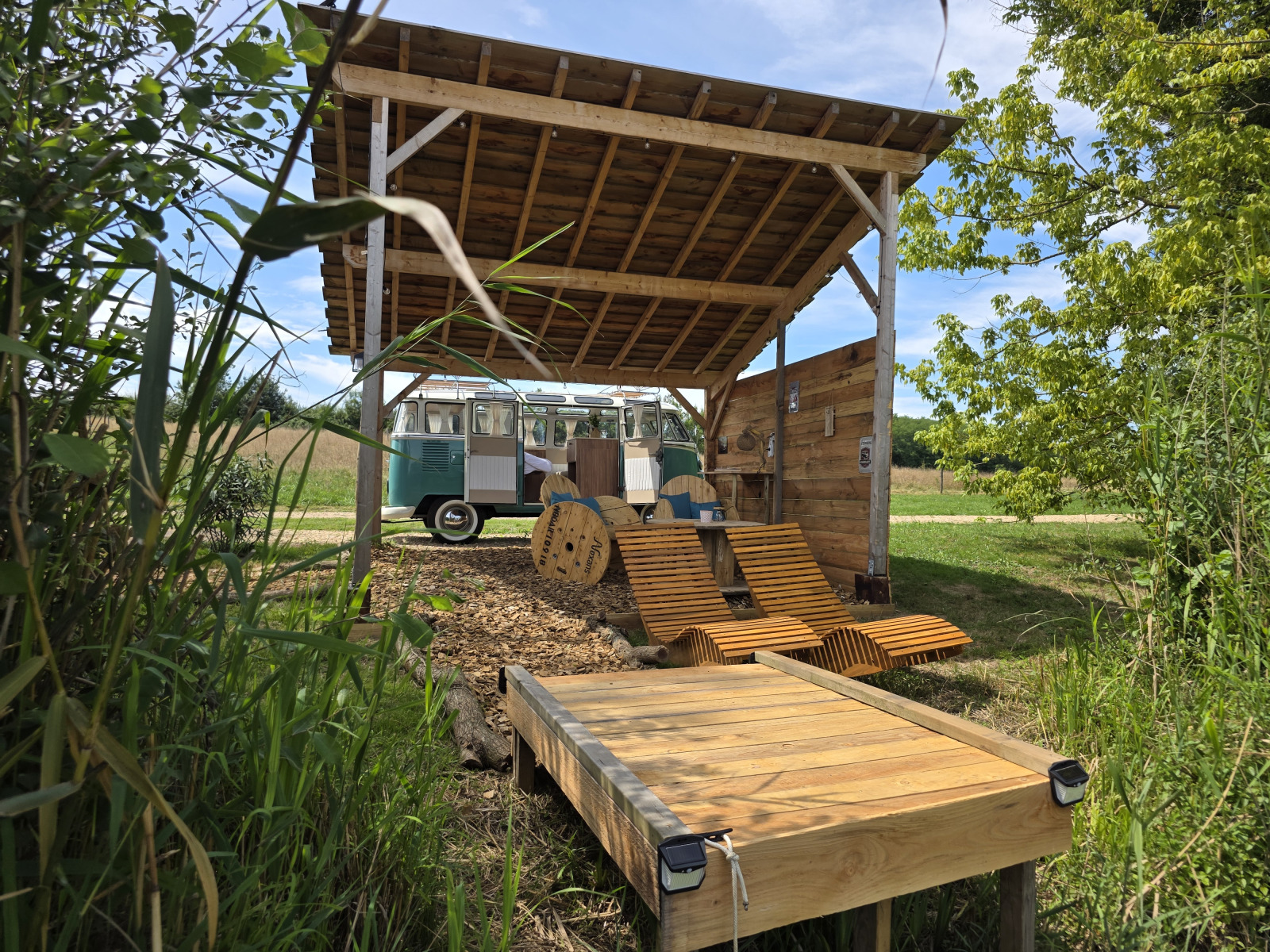 Buitenruimte met houten ligstoelen en Volkswagenbus bij Combi Harvey, Domaine des Feuilles, Frankrijk.