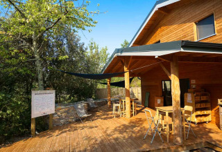 Houten buitenterras bij een hut in Bivouac nature vakantiepark in Occitanië, Frankrijk, met tafels en stoelen.
