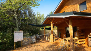 Houten buitenterras bij een hut in Bivouac nature vakantiepark in Occitanië, Frankrijk, met tafels en stoelen.