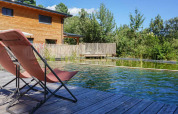Sedie a sdraio accanto a una piscina naturale e una casa di legno al Bivouac nature, Occitania, Francia.