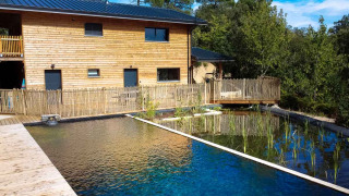 Natuurlijk zwembad en houten gebouw bij Bivouac Nature vakantiepark in Occitanië, Frankrijk, tussen de bomen.