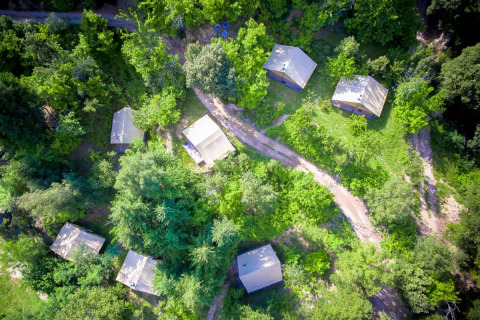 Vista aérea del parque vacacional Bivouac nature en Occitania, Francia, con cabañas entre bosque denso.