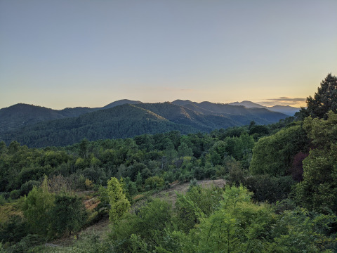 Landschaft mit grünen Hügeln und Wäldern bei Sonnenuntergang im Bivouac nature Ferienpark, Occitanie, Frankreich.