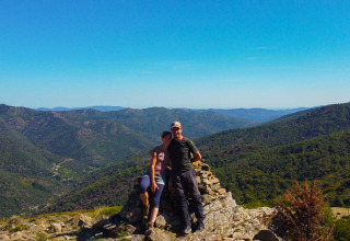 Una coppia su un punto panoramico roccioso nel parco vacanze Bivouac nature in Occitania, Francia, tra verdi colline.