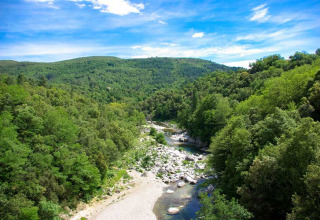 Udsigt over frodige bakker og en flod ved Bivouac Nature feriepark i Occitanie, Frankrig på en solrig dag.