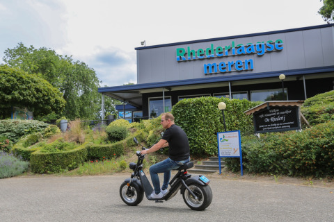 Een man rijdt op een elektrische scooter voor het gebouw van Recreatiepark Rhederlaagse Meren in Gelderland, Nederland.