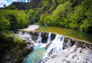 Petite cascade et rivière claire entourées de verdure près de Saint Jean du Gard, en Occitanie, France.