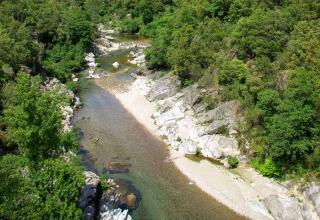 Luftaufnahme eines felsigen Flusses mit grünem Ufer bei Bivouac nature Ferienpark in Occitanie, Frankreich.