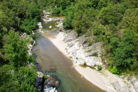 Vista aérea de un río rocoso rodeado de vegetación en el parque vacacional Bivouac nature en Occitanie, Francia.