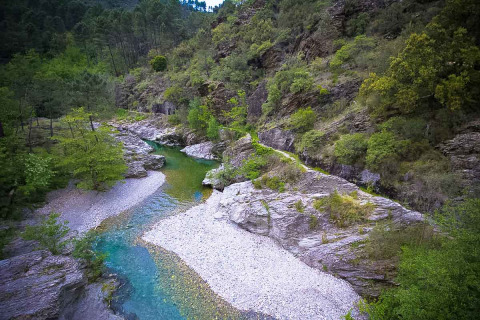 Ein klarer Fluss fließt durch Felsen und Wald im Bivouac nature Ferienpark in Okzitanien, Frankreich.