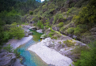 Río de aguas claras entre rocas y bosque en el parque vacacional Bivouac nature en Occitania, Francia.