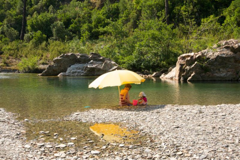Due persone sedute sotto un ombrellone giallo sulla riva di un fiume a Saint Jean du Gard, Occitania, Francia.