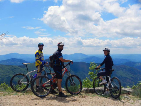 Trois cyclistes avec casques profitent de la vue sur les montagnes au parc de vacances Bivouac nature, Occitanie, France.
